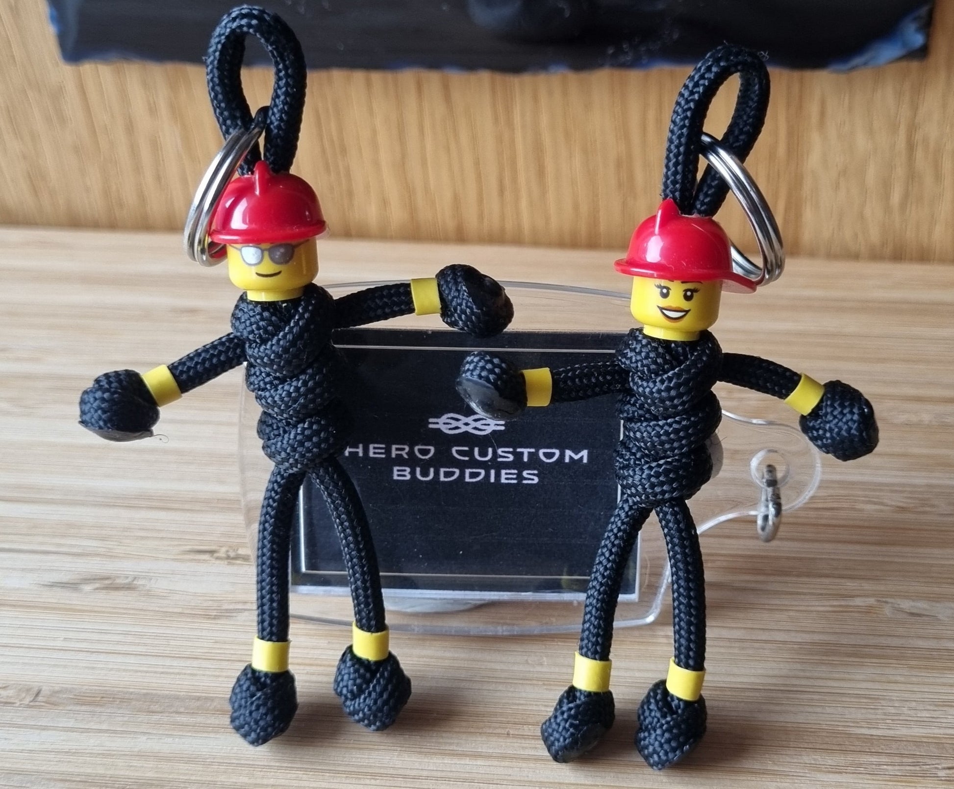 Male and female firefighter keychains made with black paracord and red building block helmets