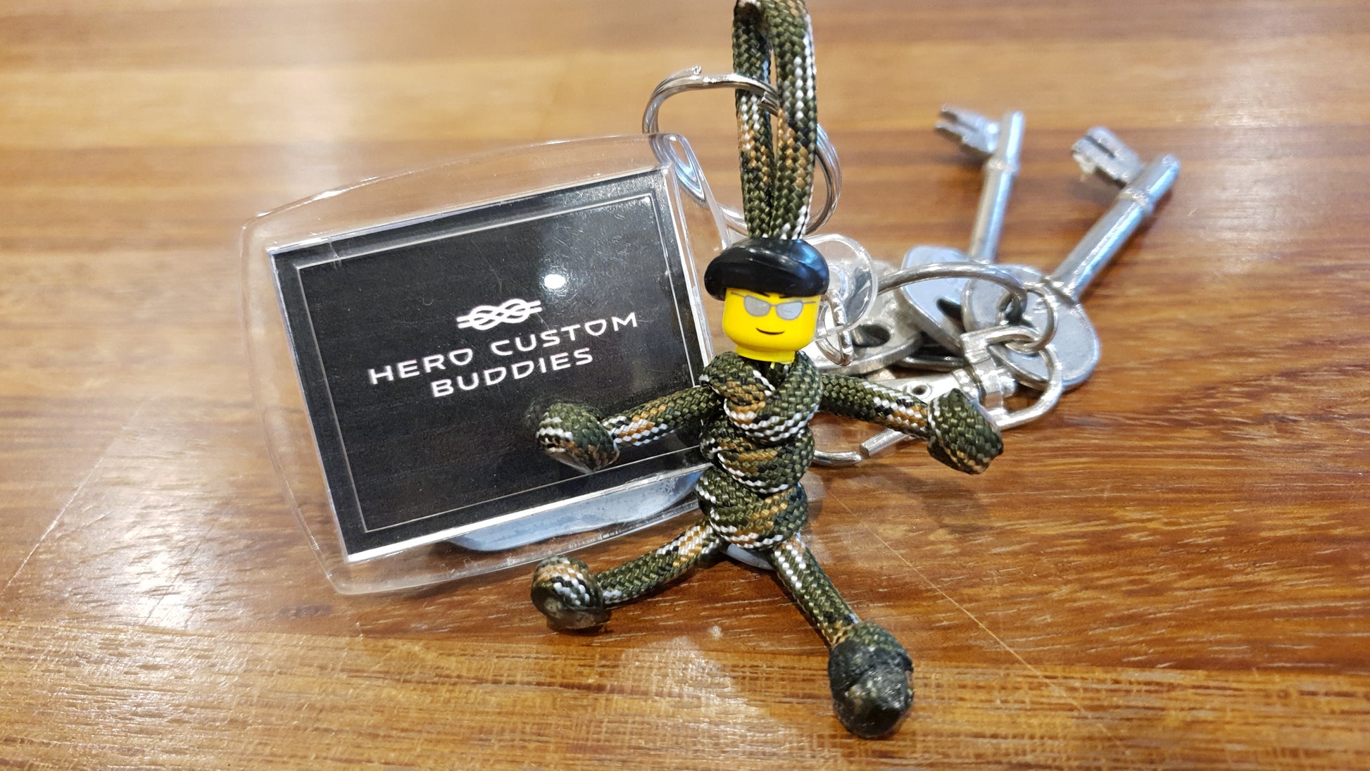 keychain made from army camouflage coloured paracord and yellow building block head wearing sunglasses and a black beret. Paracord is styled with snake knots to look like a little army soldier.