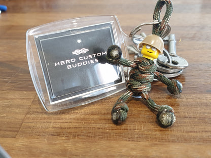 keychain made with army camouflage coloured paracord with a yellow building block head and a beige army helmet